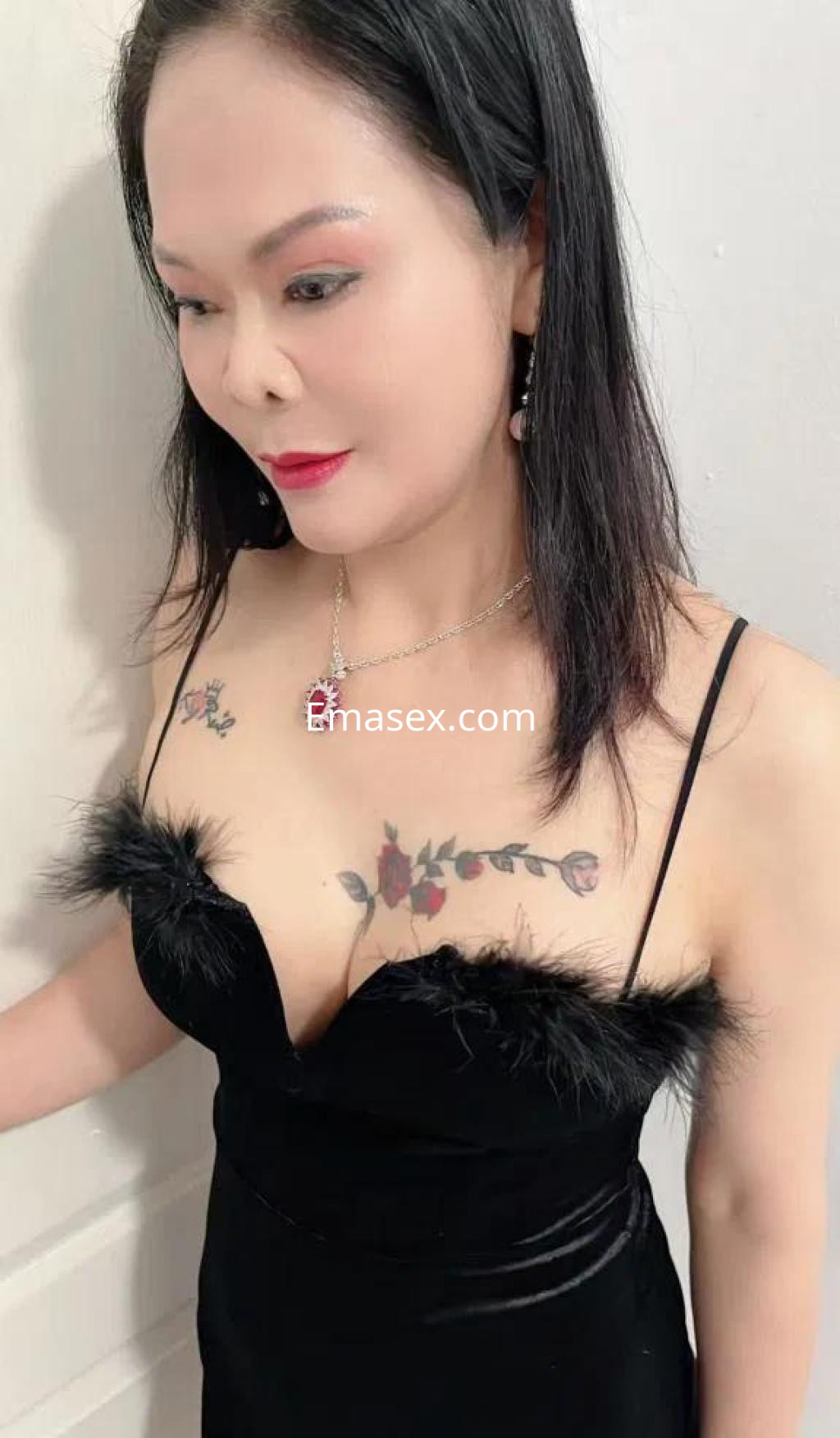 Puta en Barcelona con vestido negro de tirantes, detalles de plumas y tatuajes visibles en el escote.