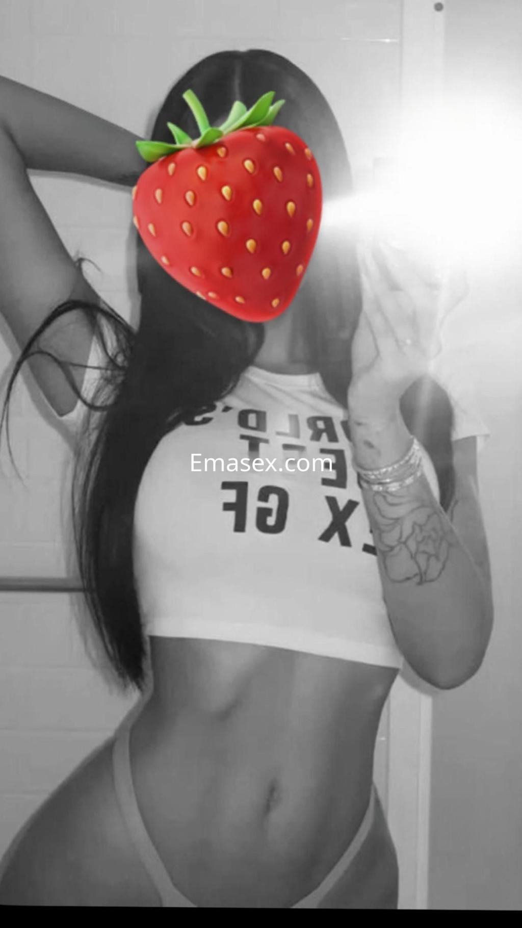 Escort en Huelva posando frente al espejo con una camiseta ajustada y lencería, mostrando su figura esbelta.