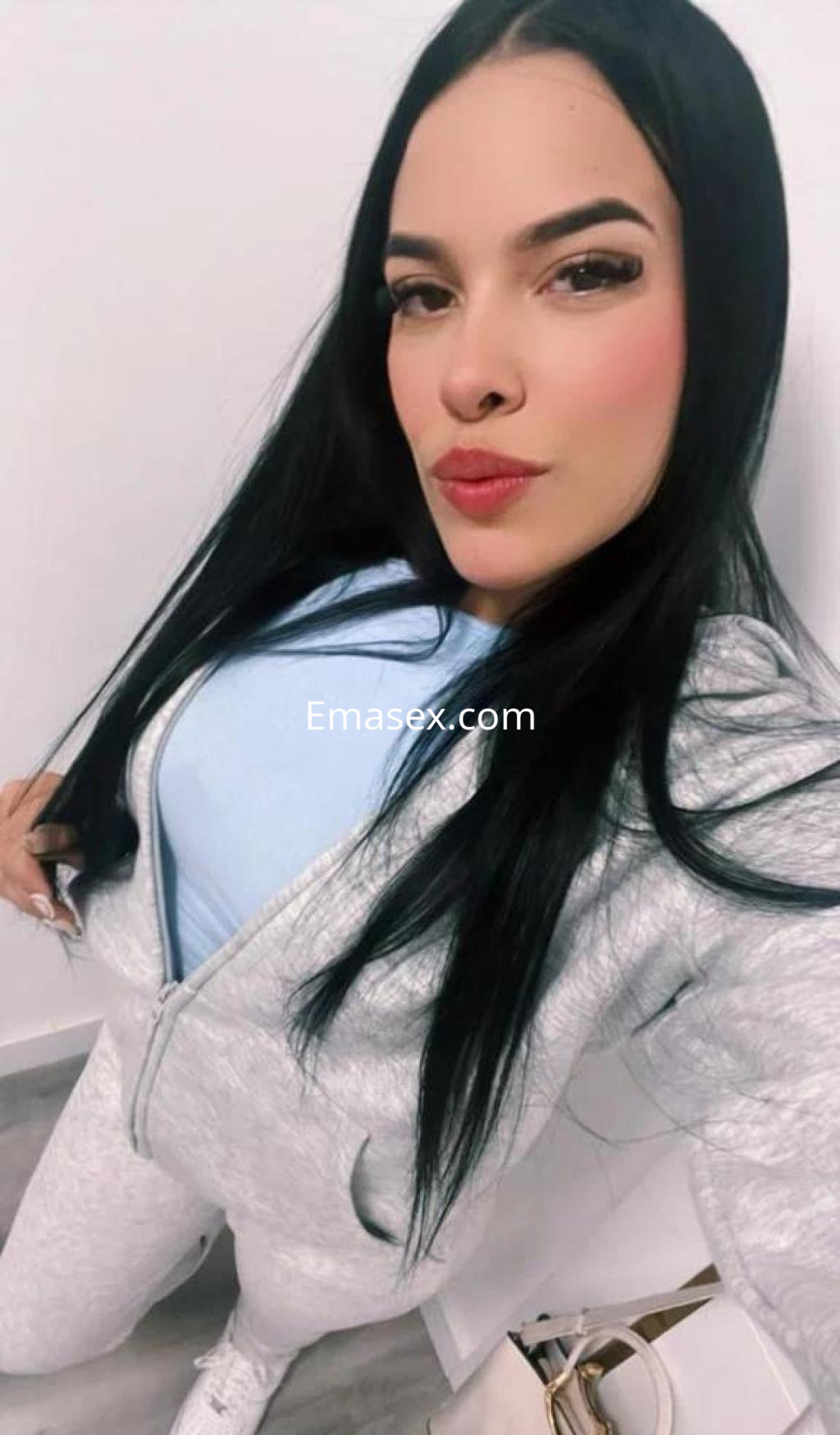 Puta con cabello largo y lacio, viste un conjunto deportivo gris y posa con una expresión coqueta en León.