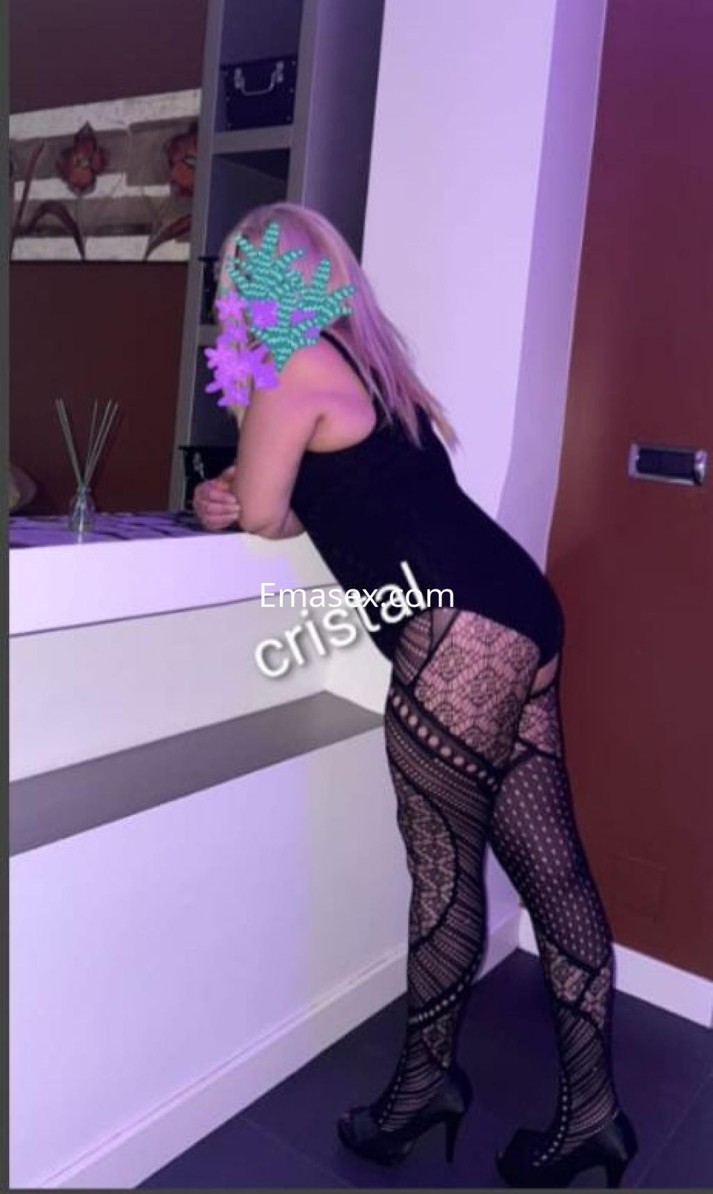 La puta en Lugo lleva un vestido negro ajustado y medias de red, posando junto a una barra moderna.