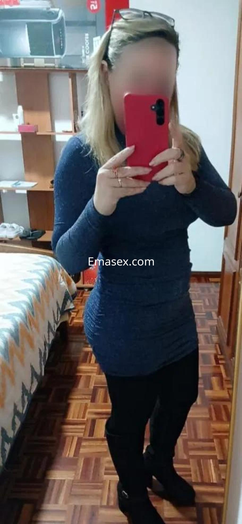 Escort en Pontevedra posando frente al espejo con un vestido azul oscuro y leggings negros en un entorno interior.