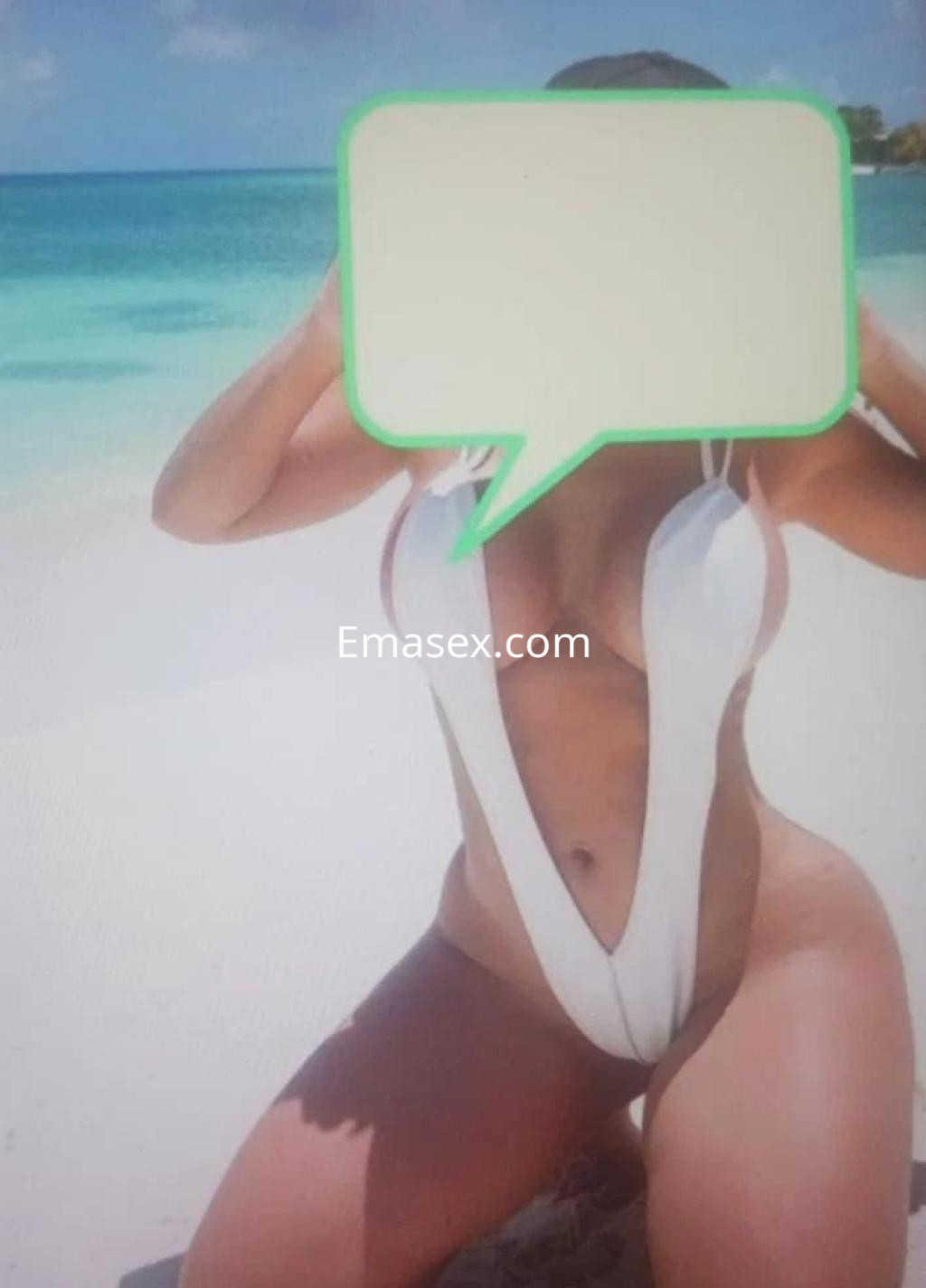 Escort en Salamanca posando en la playa con un traje de baño blanco, de fondo se aprecia el mar y la arena.
