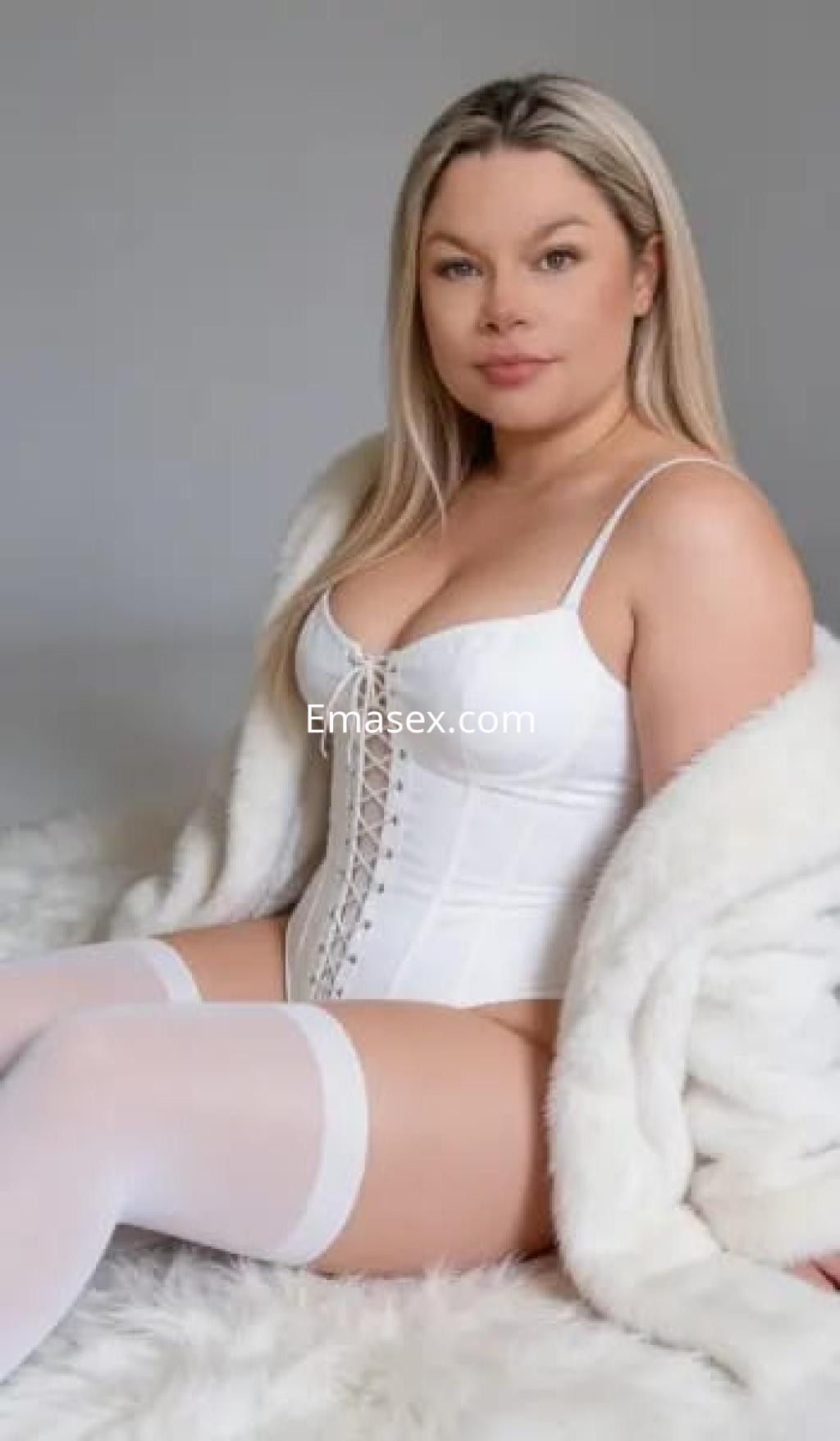 Escort en Salamanca con cabello rubio, viste un corsé blanco y medias, rodeada de una suave manta blanca.