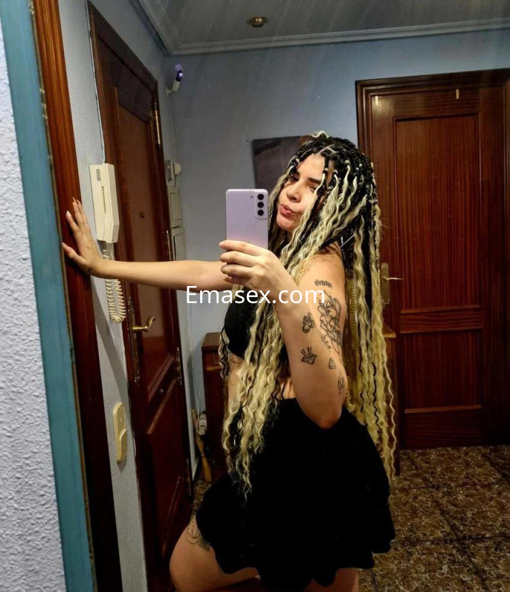 Puta con cabello trenzado y rubio, vistiendo una blusa negra y falda corta, posando en un espejo en Zaragoza.