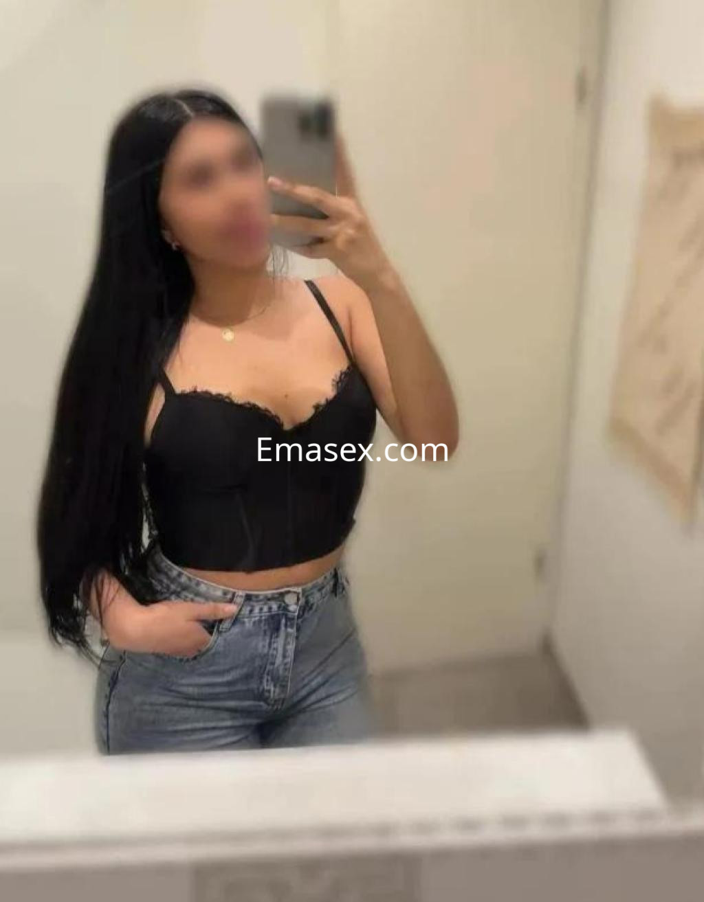 Escort en Zaragoza con cabello largo y oscuro, vestida con top negro y jeans, posando frente al espejo.