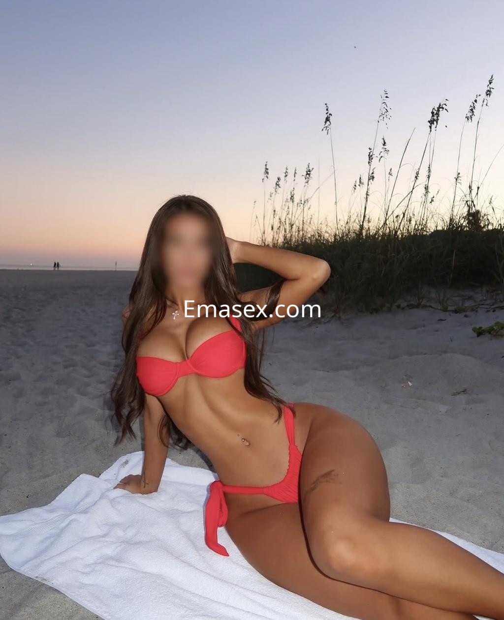 Escort en Donosti posando en la playa al atardecer, viste un bikini rojo y tiene el cabello largo y suelto.