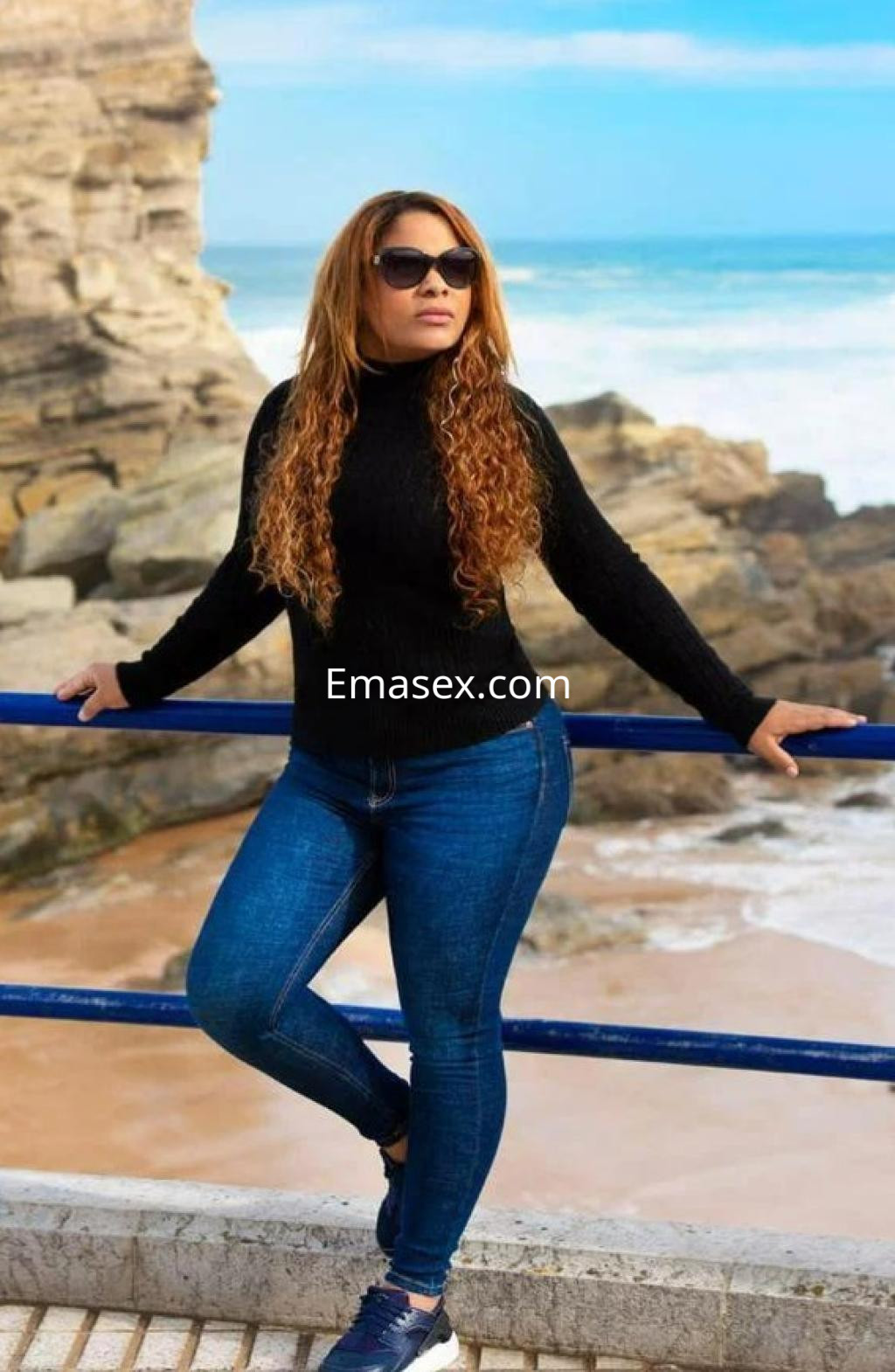 Puta con cabello largo y rizado, viste un suéter negro y jeans ajustados, posando en la costa de Zaragoza.