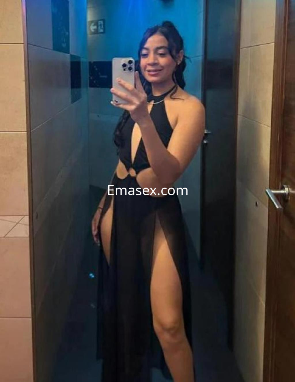 Escort en Zaragoza con un vestido negro transparente que destaca sus piernas, posando frente a un espejo.