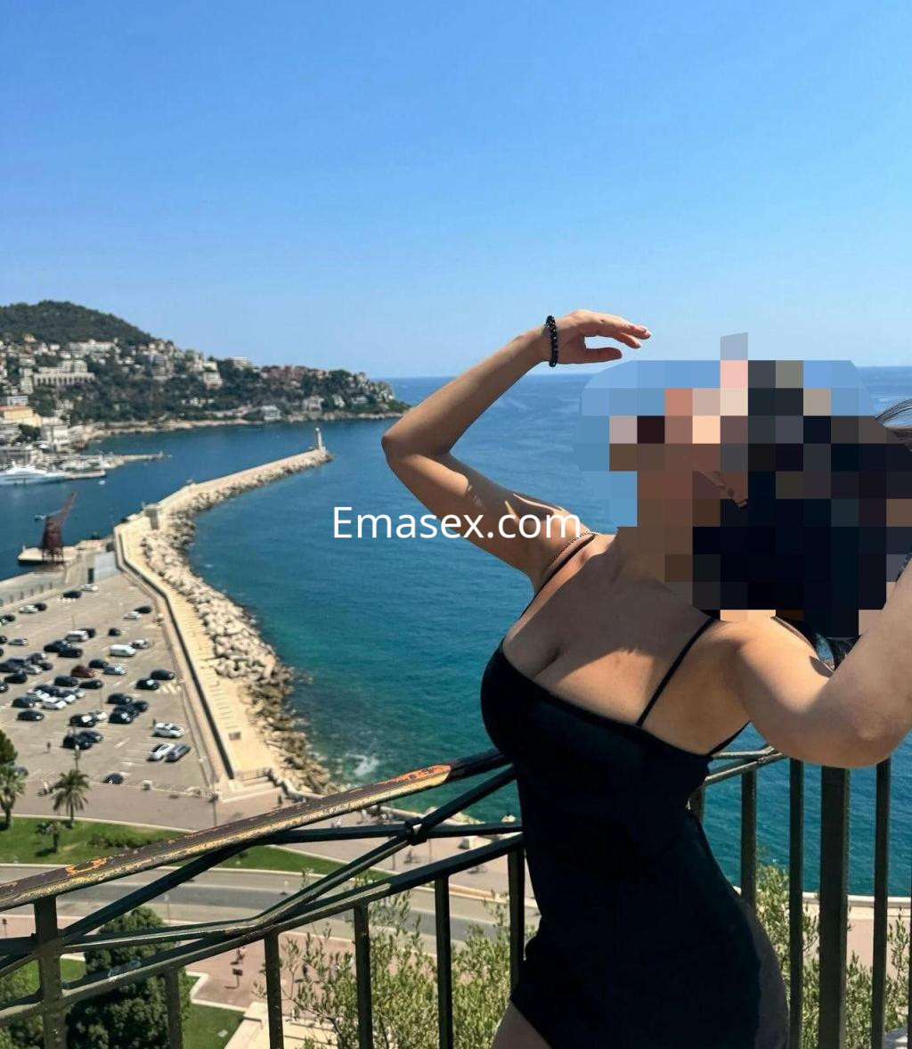 La puta posa en un vestido negro, disfrutando de una vista panorámica del mar en Albacete.