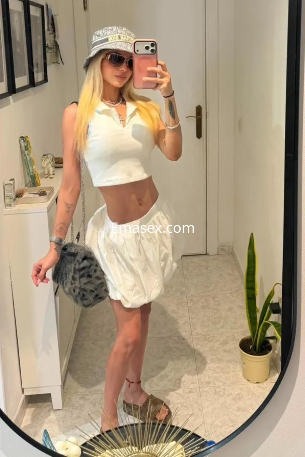Escort en Palma de Mallorca, luciendo un top blanco y una falda corta, con un sombrero y bolso de pelaje.