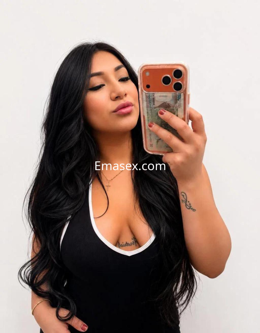 Escort en Madrid con cabello largo y oscuro, vistiendo un ajuste ceñido y tomando una selfie en un fondo claro.