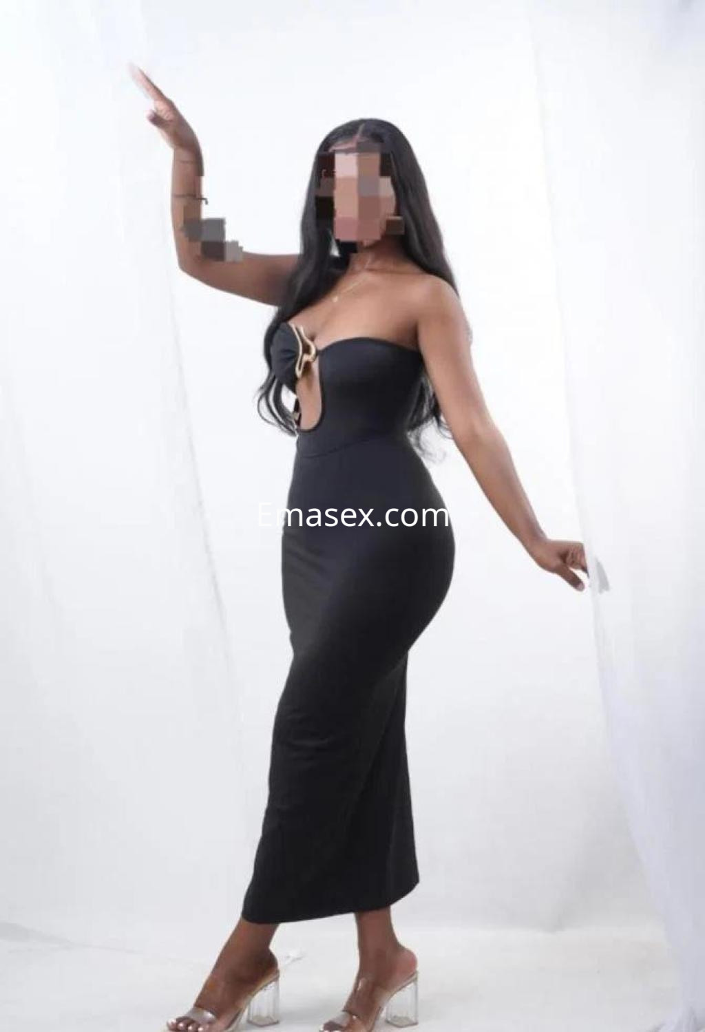 Escort en Tarragona posando con un vestido negro ajustado y sandalias transparentes, con cabello largo y suelto.