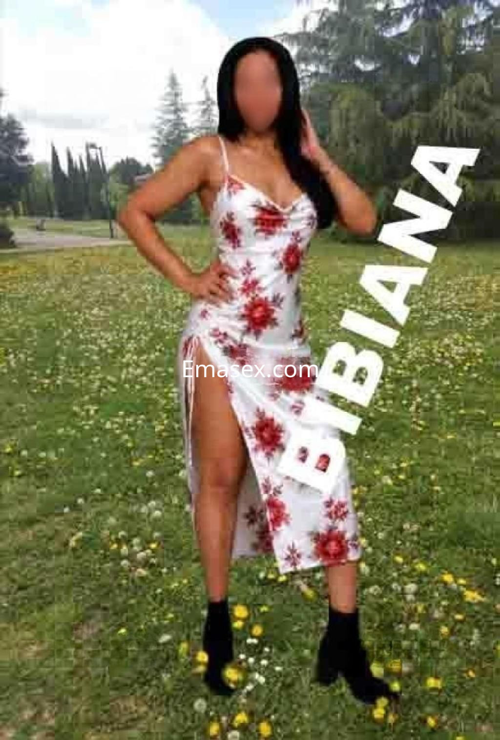Escort en Valladolid luciendo un vestido floral de tirantes, posando en un entorno natural con césped y flores.