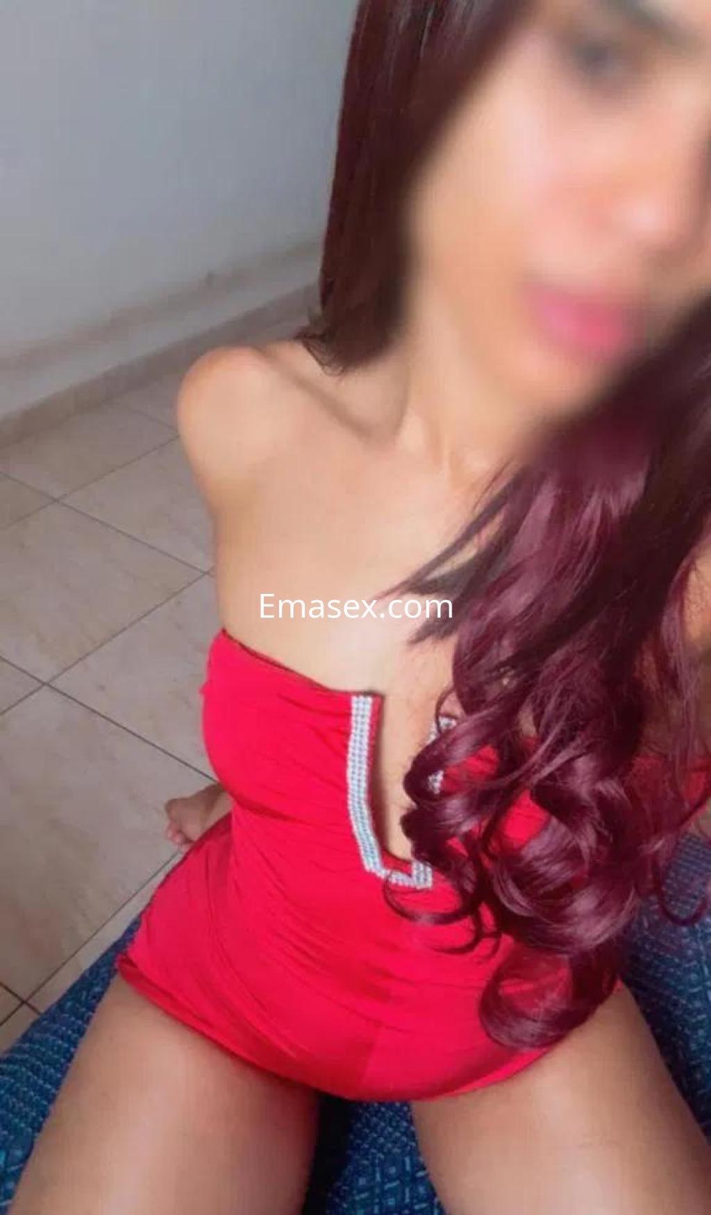 Puta sentada en un sofá, lleva un vestido rojo con escote y tiene el cabello largo y ondulado en Zamora.