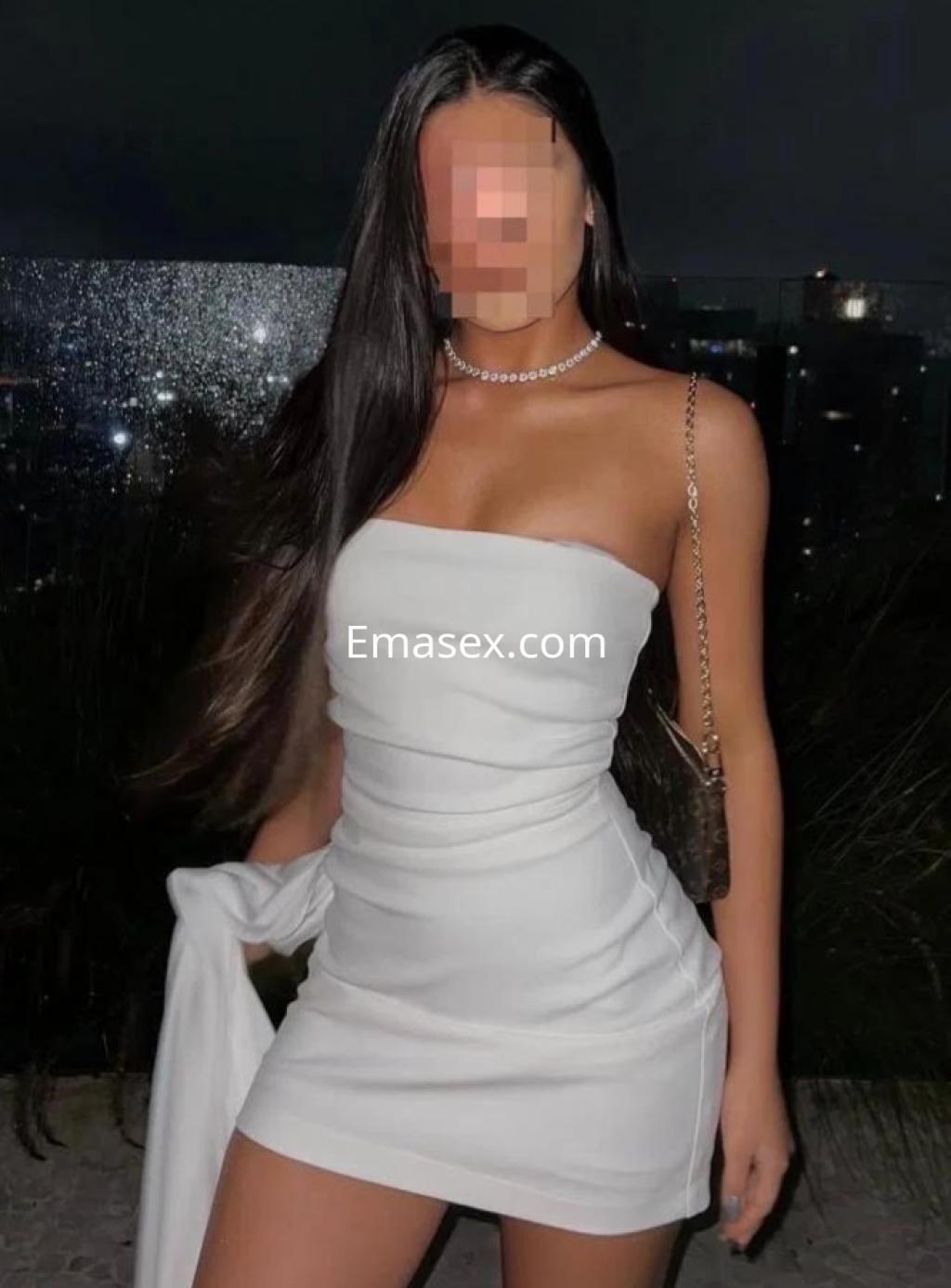 Escort en Pamplona con vestido blanco ajustado, cabello largo y lacio, posando en un entorno nocturno iluminado.