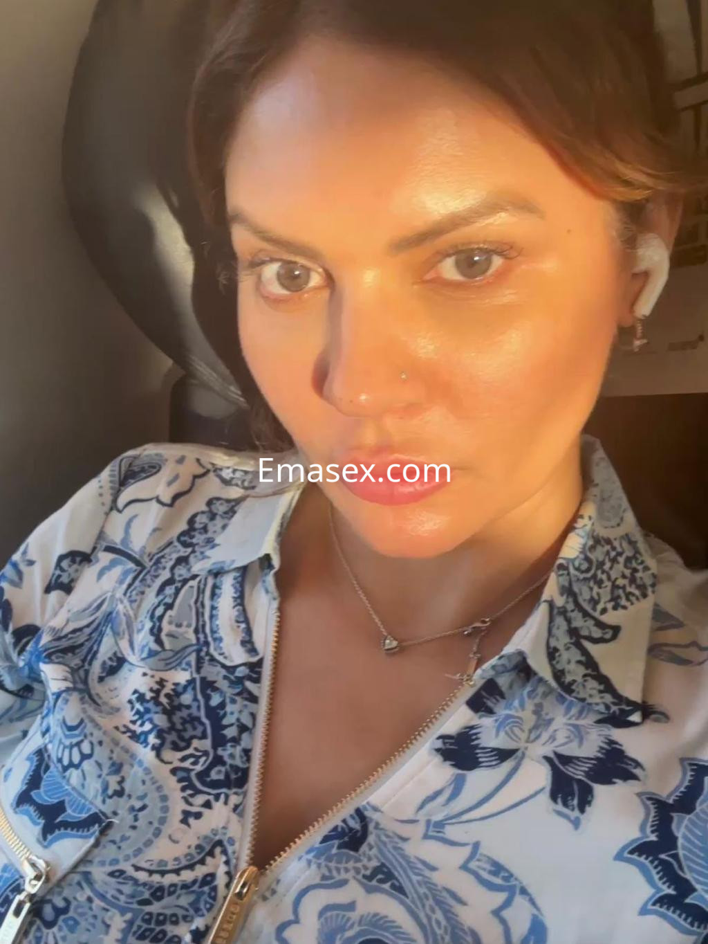 Puta con blusa estampada en azul y blanco, luciendo un maquillaje natural y peinado con ondas, en un avión.