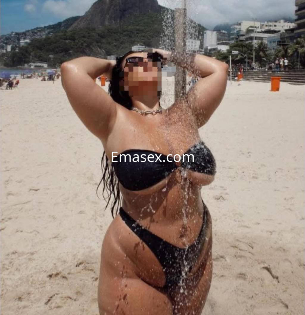 Escort en Palma de Mallorca luciendo un bikini negro mientras se ducha bajo el sol en la playa.