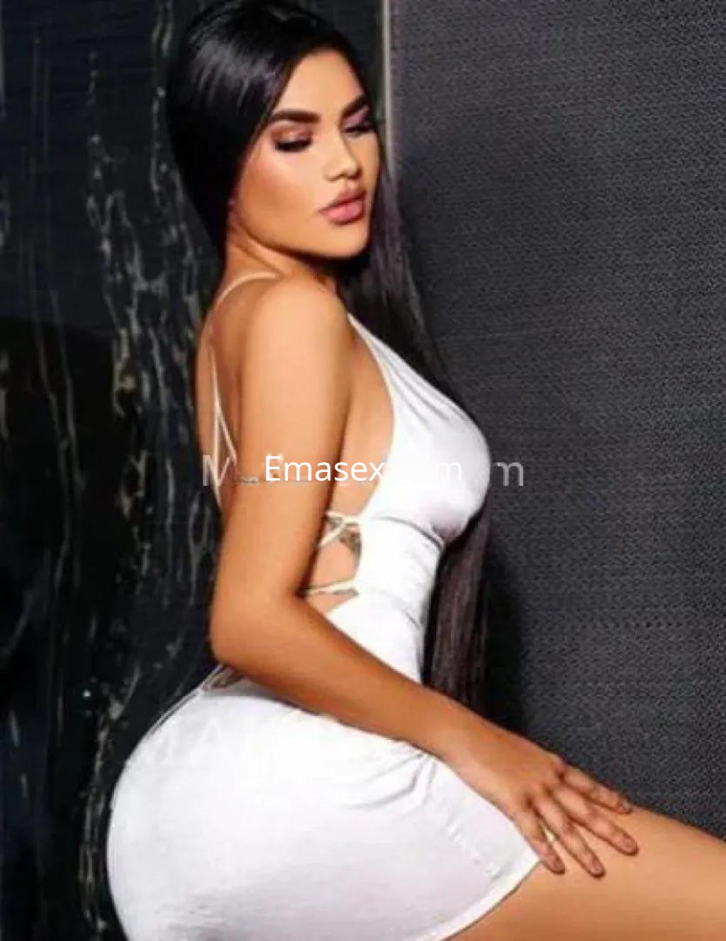 Escort en Palma de Mallorca posando de perfil con un vestido blanco ajustado y cabello largo y lacio.