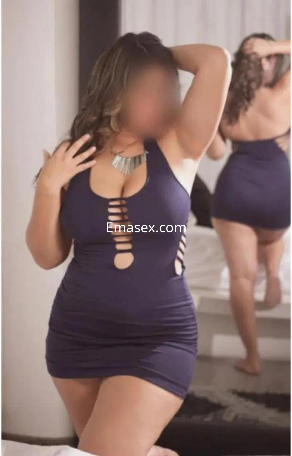 Escort posando en Barcelona, vistiendo un vestido ajustado azul con cortes, en un entorno de habitación moderna.