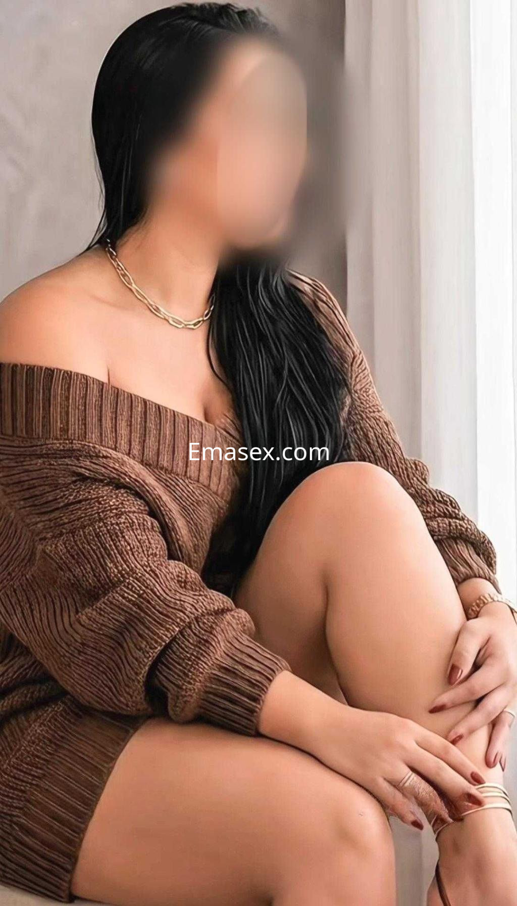 La puta luce un suéter marrón de gran tamaño, con el cabello oscuro y lacio, sentada en un ambiente acogedor en Cáceres.