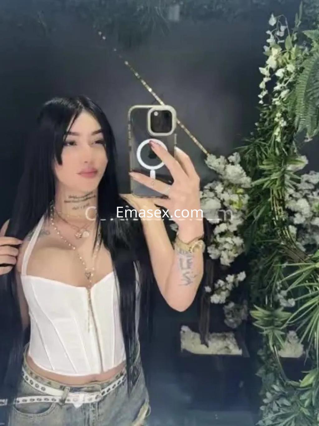 Escort en Córdoba con cabello largo y oscuro, viste un corset blanco y jeans cortos, posando frente a un espejo.