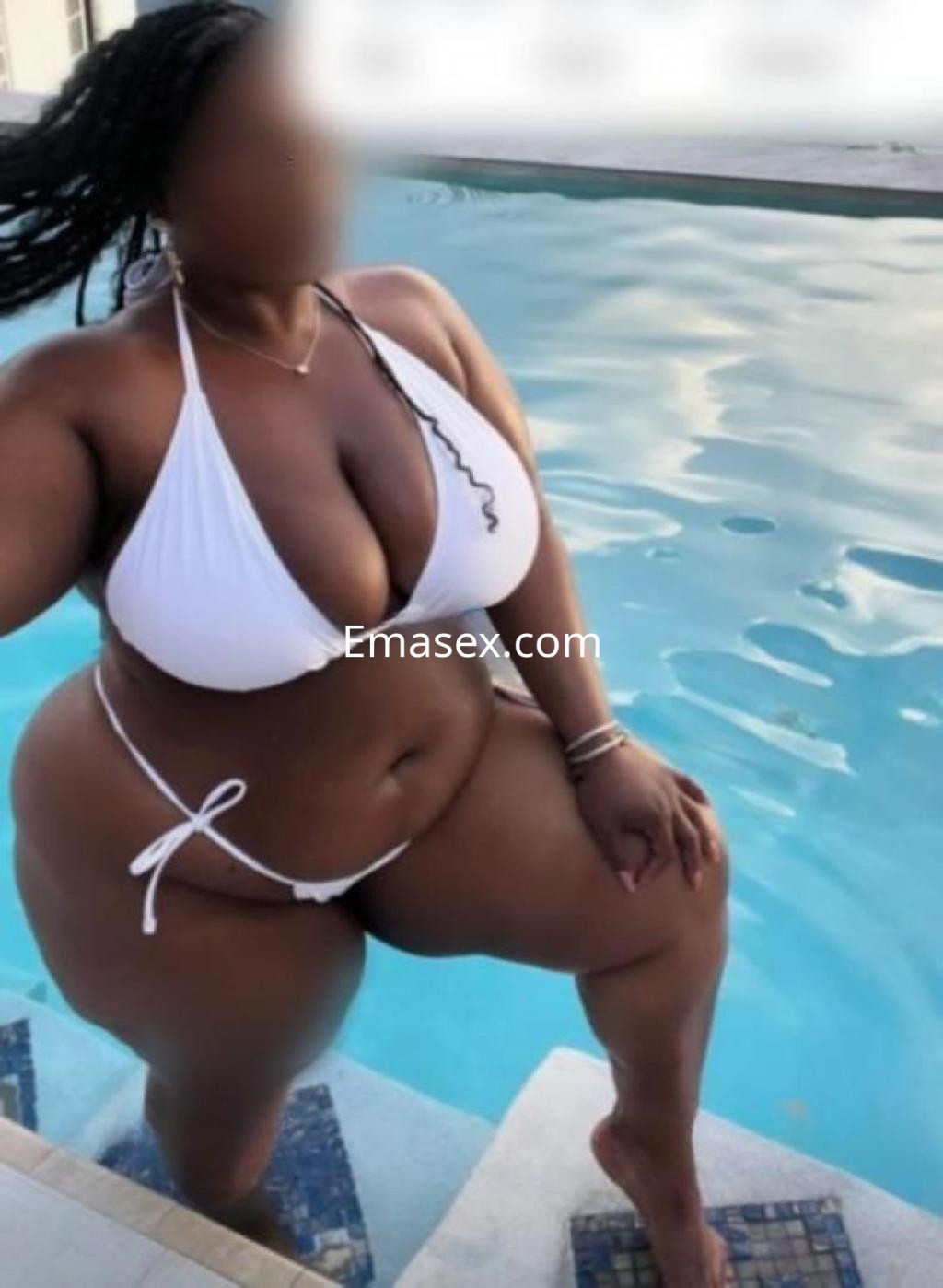 Escort posando junto a una piscina, vistiendo un bikini blanco y con cabello trenzado en Huelva.
