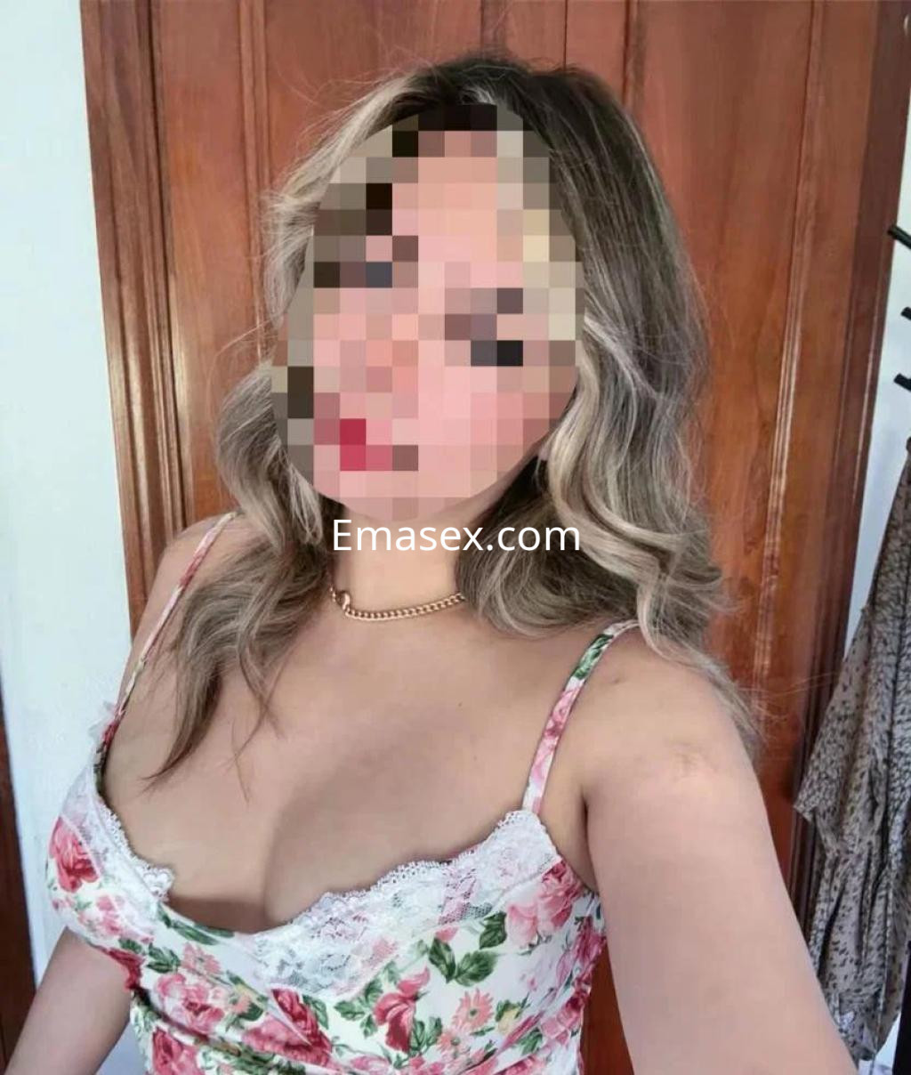 Escort posa con blusa de tirantes floral, cabello ondulado y un fondo de madera en León.
