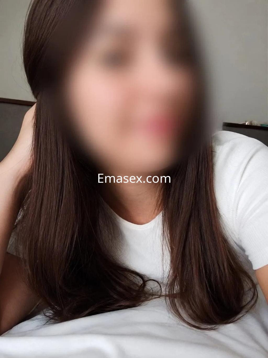 Escort en Madrid con cabello largo y castaño, luciendo una camiseta blanca mientras se relaja en un entorno interior.