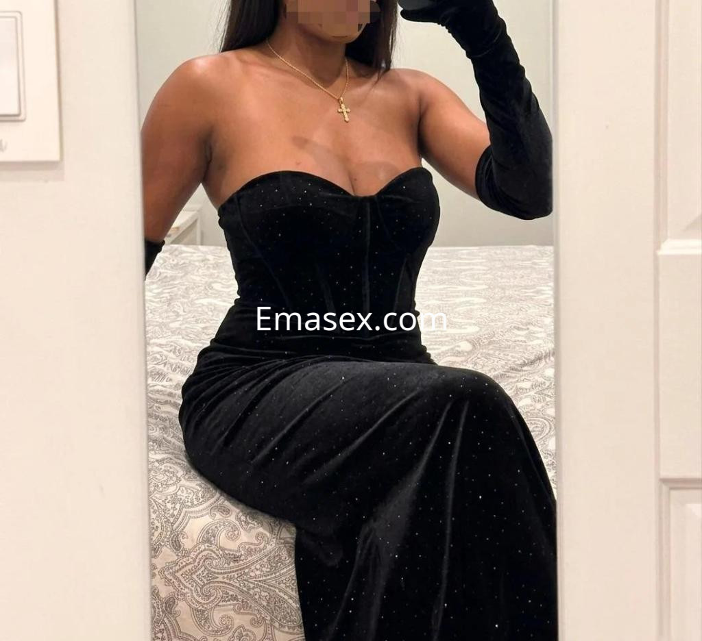 Escort en Madrid con un vestido negro ajustado y guantes largos, posando frente a un espejo.