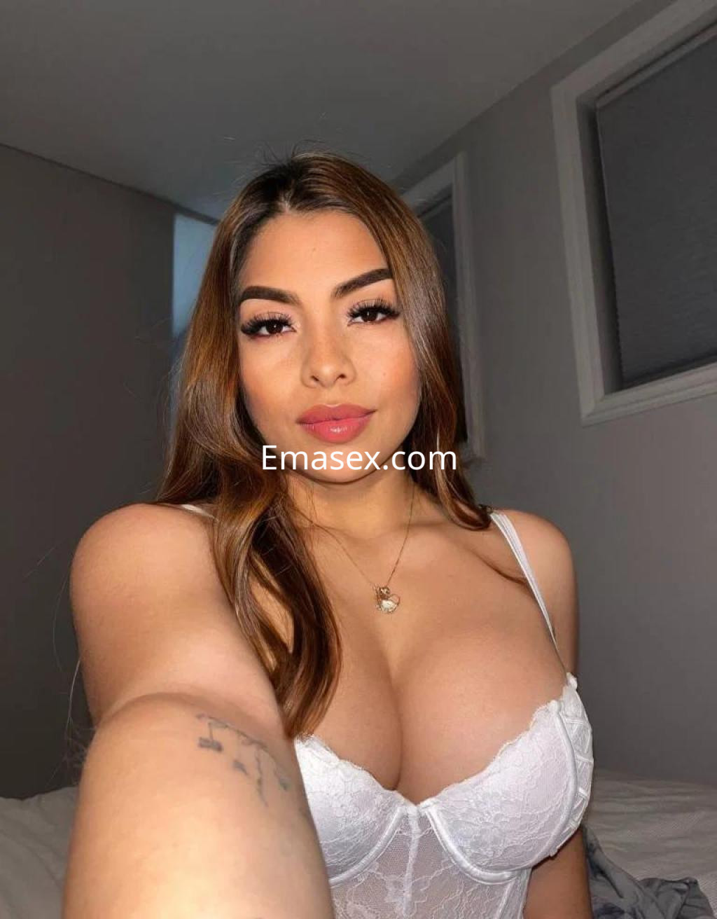 Escort en Madrid con cabello largo y lacio, luciendo un sujetador blanco y posando con una sonrisa en un ambiente interior.