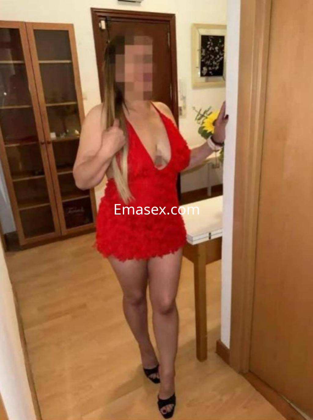 Escort en Madrid con vestido rojo de flores, tacones altos y cabello largo, posando en un interior luminoso.