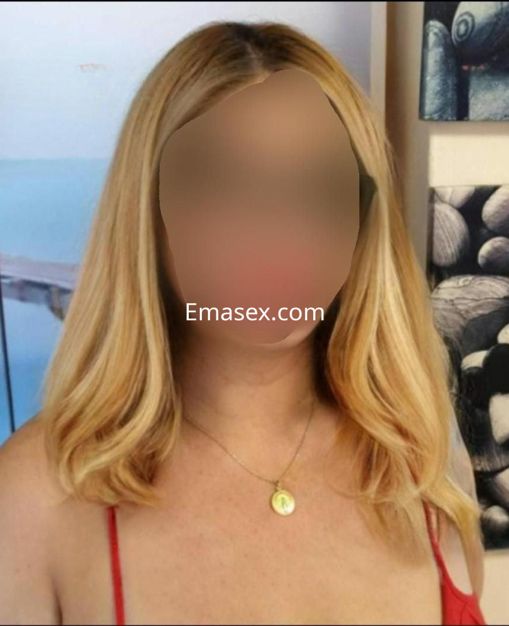 Escort en Zaragoza con cabello rubio ondulado, luciendo un vestido rojo y un collar sencillo, en un entorno decorativo.