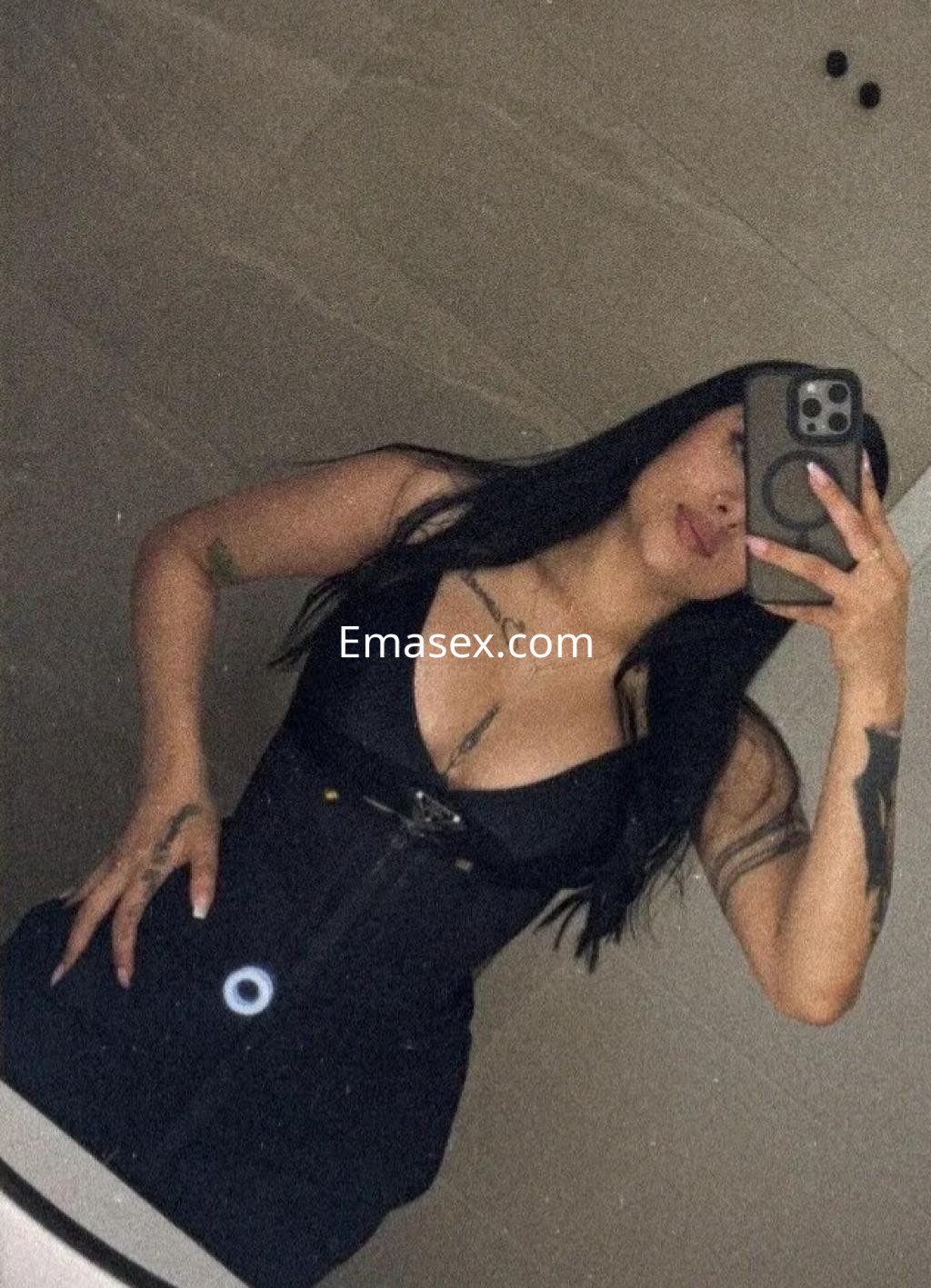 Escort en Valencia con cabello largo y oscuro, vistiendo un vestido ajustado negro, posando frente al espejo.