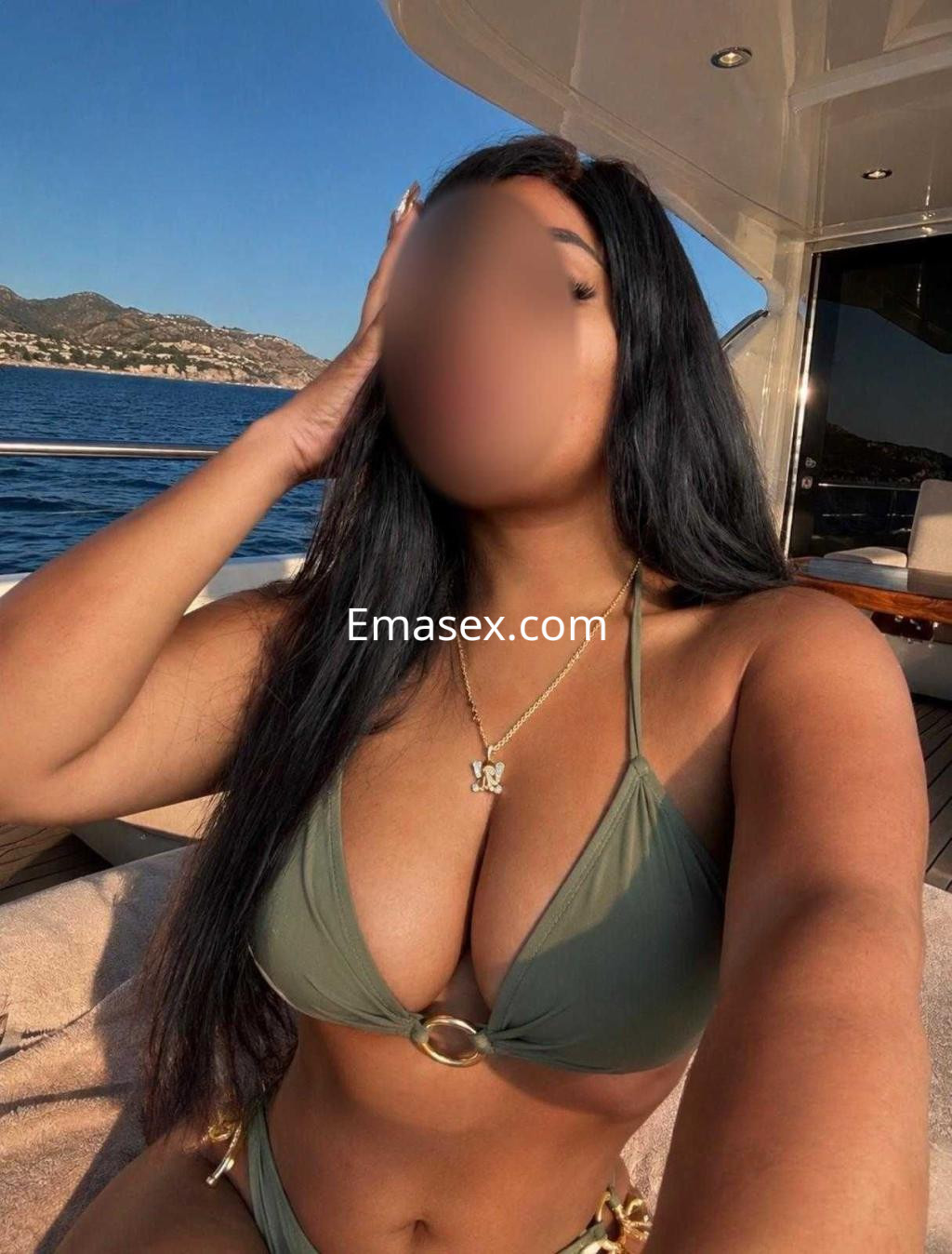 Escort de Barcelona con piel bronceada, cabello largo y lacio, luciendo un bikini verde en un yate junto al mar.