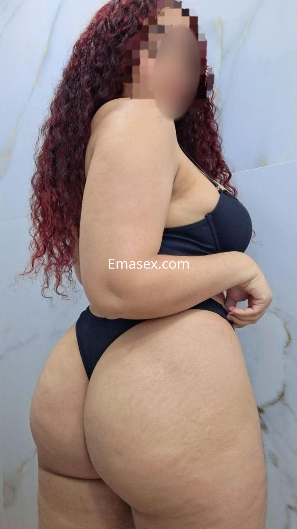Escort en Barcelona posando de perfil, con cabello rizado y un traje de baño negro, destacando su figura.