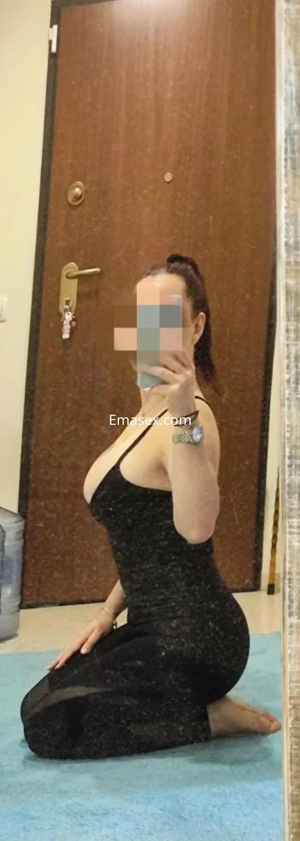 Puta en Cáceres, posando de rodillas frente al espejo con un vestido negro ajustado y cabello recogido.