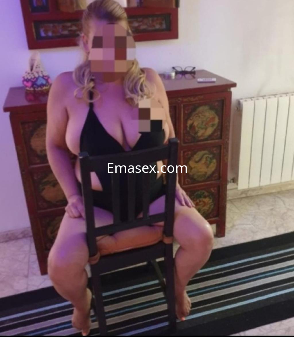 Puta sentada en una silla con un traje de baño negro, en un ambiente acogedor de Coruña.