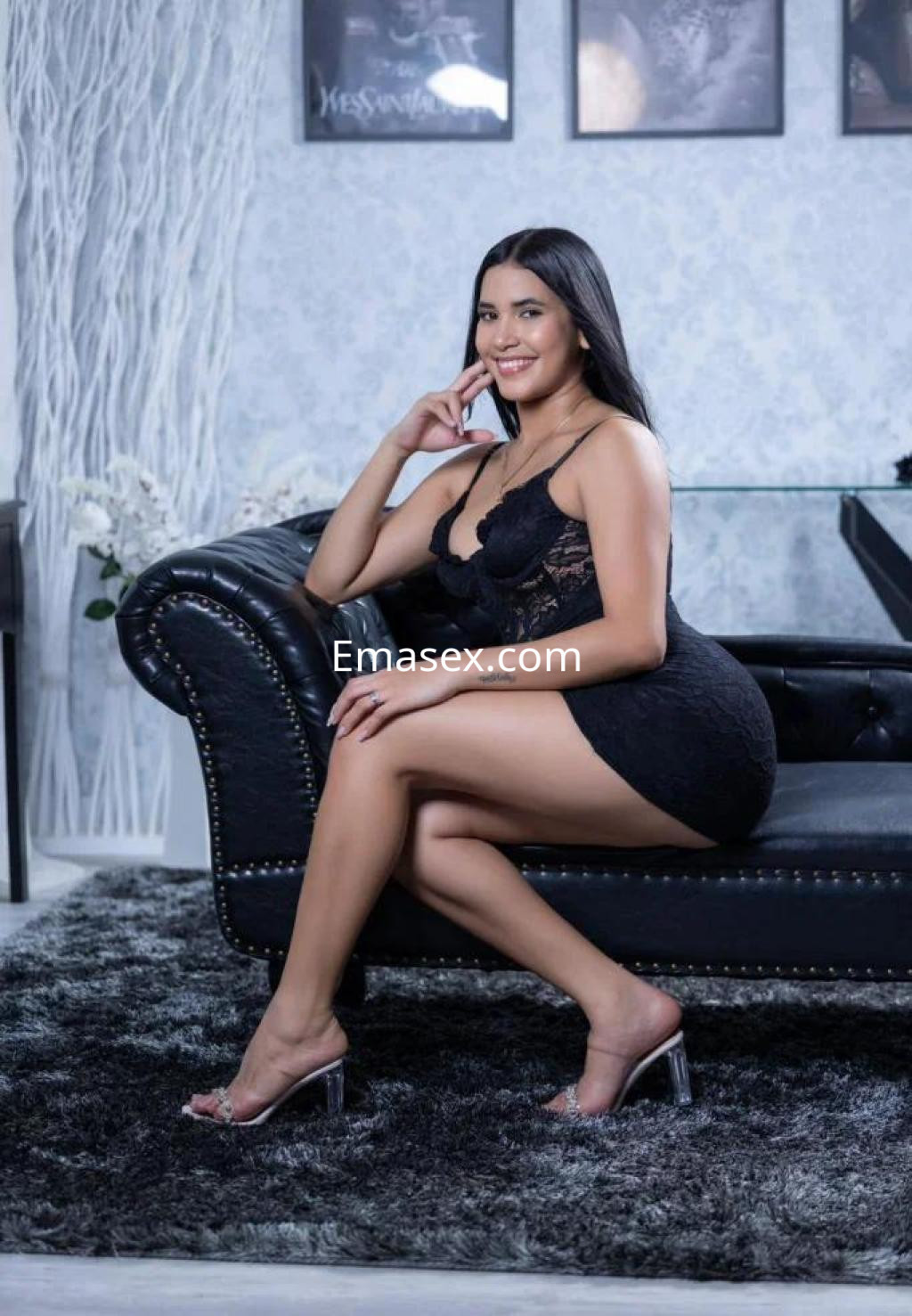 Puta posando con un vestido negro ajustado y tacones transparentes en un sofá elegante en Girona.