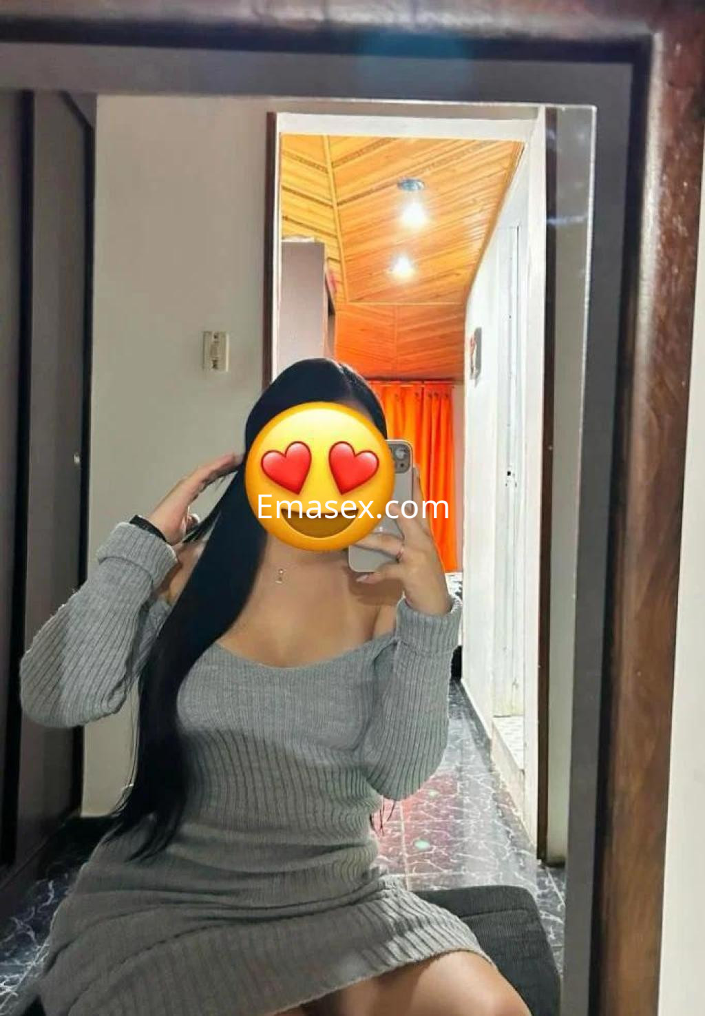 Puta sentada frente a un espejo, luciendo un vestido gris y con cabello largo y lacio en un ambiente de León.