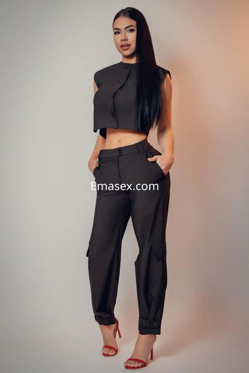 Escort en Madrid con cabello largo y lacio, viste un conjunto de dos piezas en tonos oscuros y sandalias rojas.