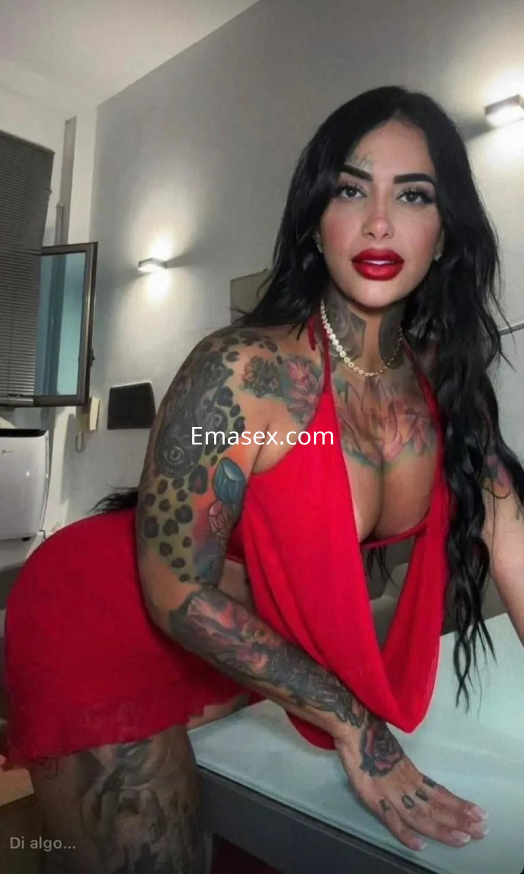 Puta con cabello largo y oscuro, vistiendo un vestido rojo, posando en un entorno moderno en Madrid.