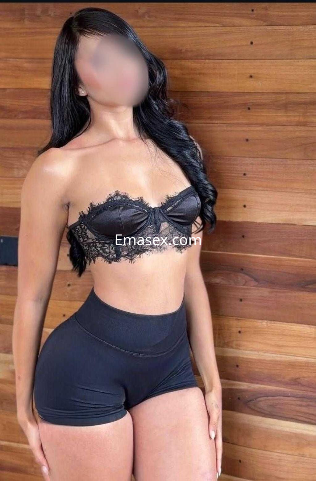 Escort en Madrid con top negro de encaje y shorts ajustados, posando en un entorno de madera.