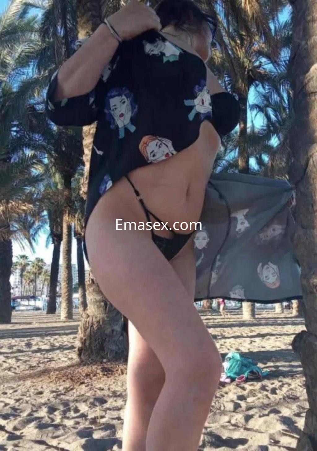 Escort en Málaga con cabello oscuro, vistiendo un pareo transparente sobre un bikini en la playa.