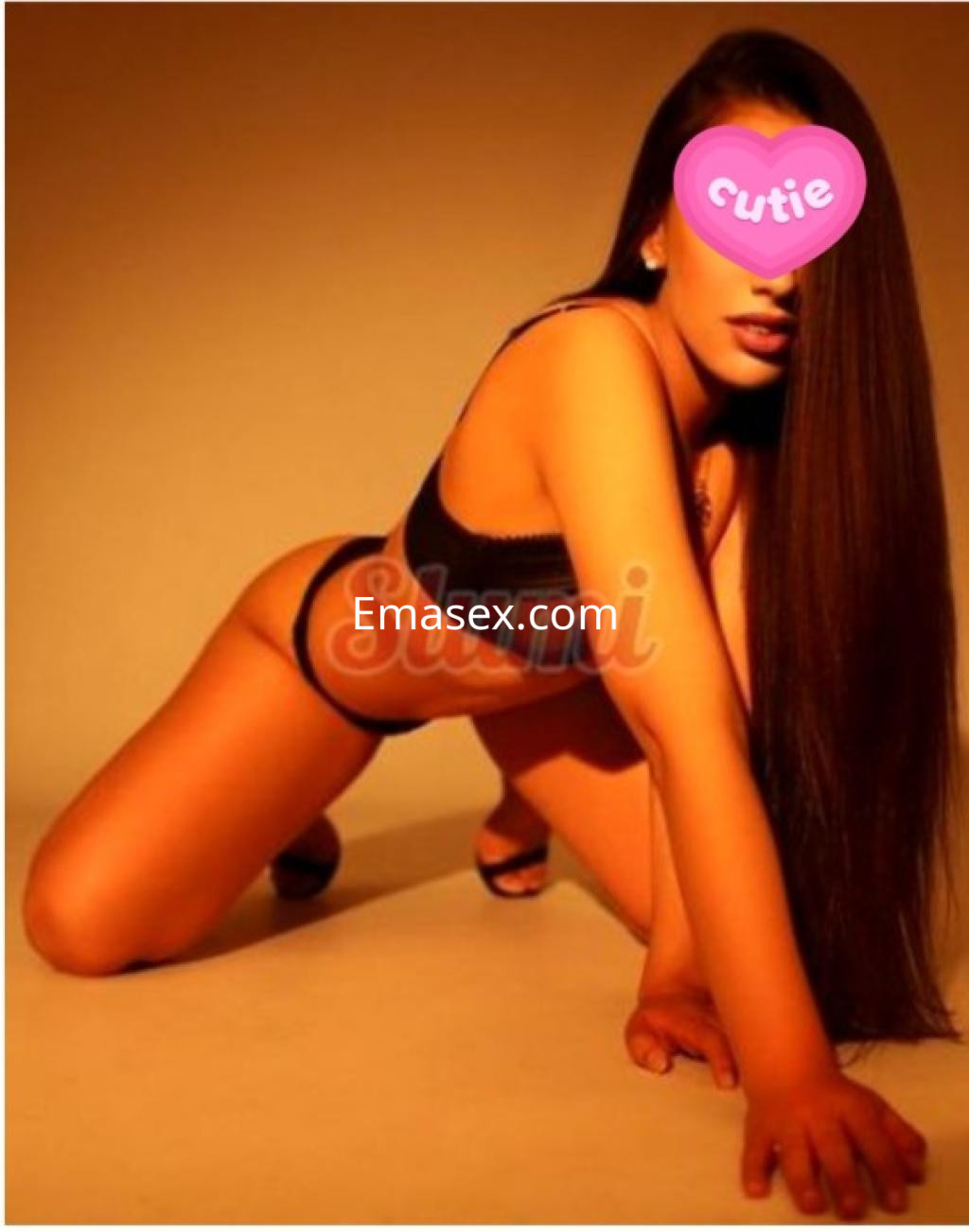 Escort en Vigo posando de rodillas, con cabello largo y lacio, vistiendo lencería negra y tacones.