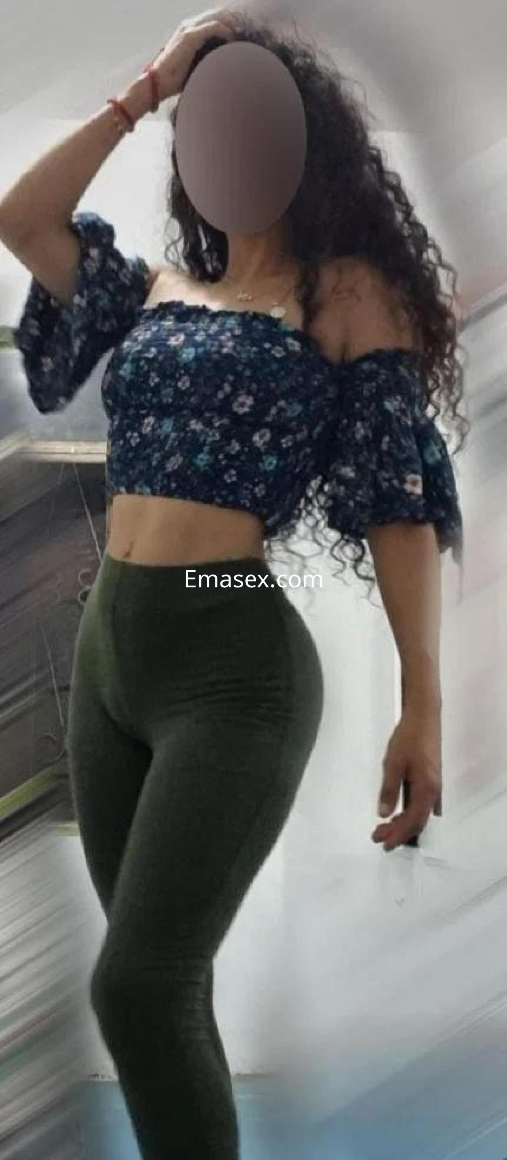 Puta de cabello rizado y oscuro, viste blusa floral sin mangas y leggins verdes, posando en un ambiente interior en Toledo.