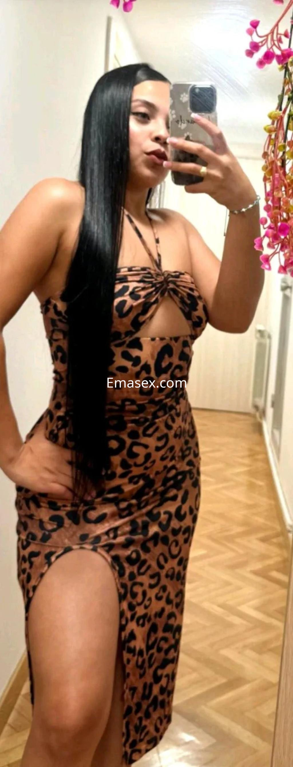 Escort en Zaragoza con cabello largo y lacio, lleva un vestido de leopardo y posa frente a un espejo en un pasillo.