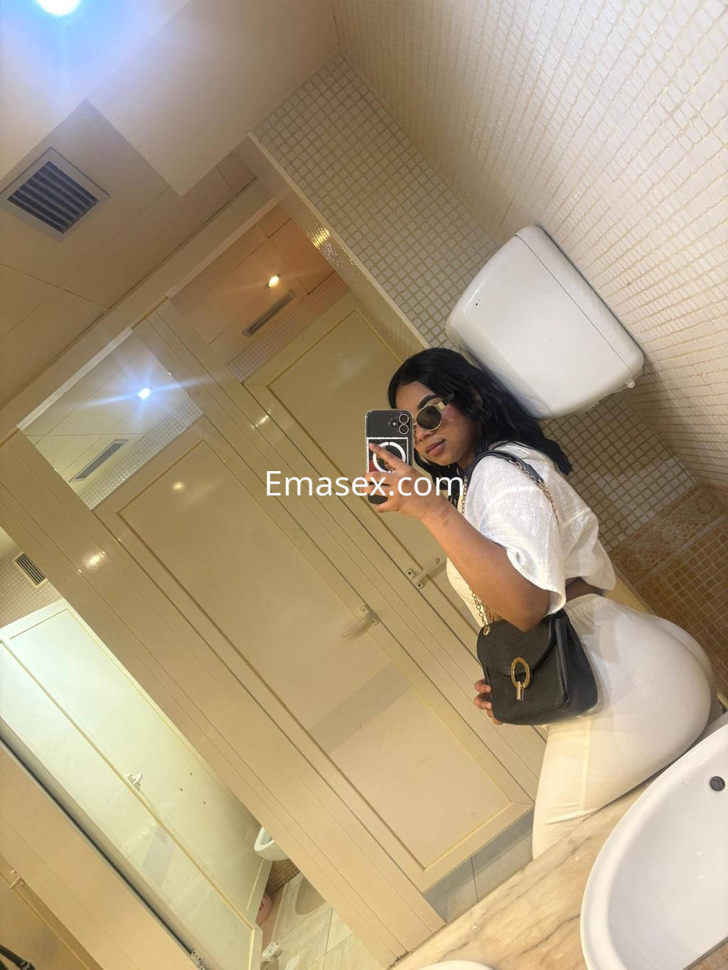 Puta en Madrid, con cabello oscuro y rizado, viste un conjunto blanco y gafas de sol, posando en un baño.