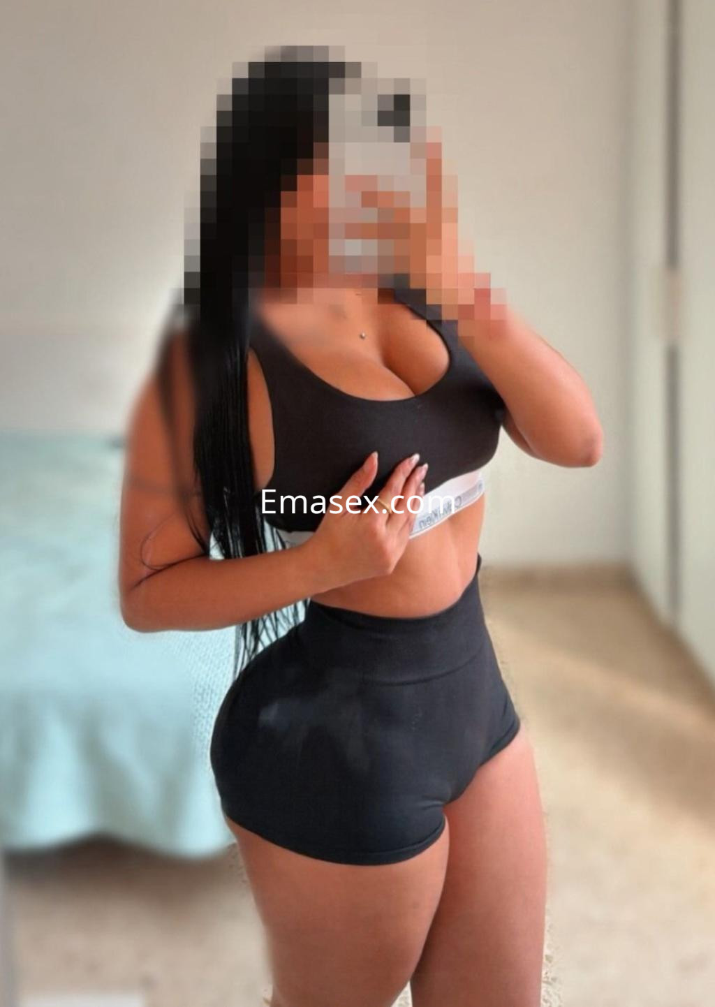 Escort en Málaga posando con un top negro ajustado y shorts, mostrando su figura en un entorno interior.