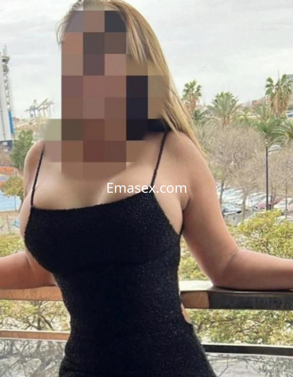 Escort en Madrid con vestido negro ajustado y tirantes, posando en un balcón con paisaje urbano.