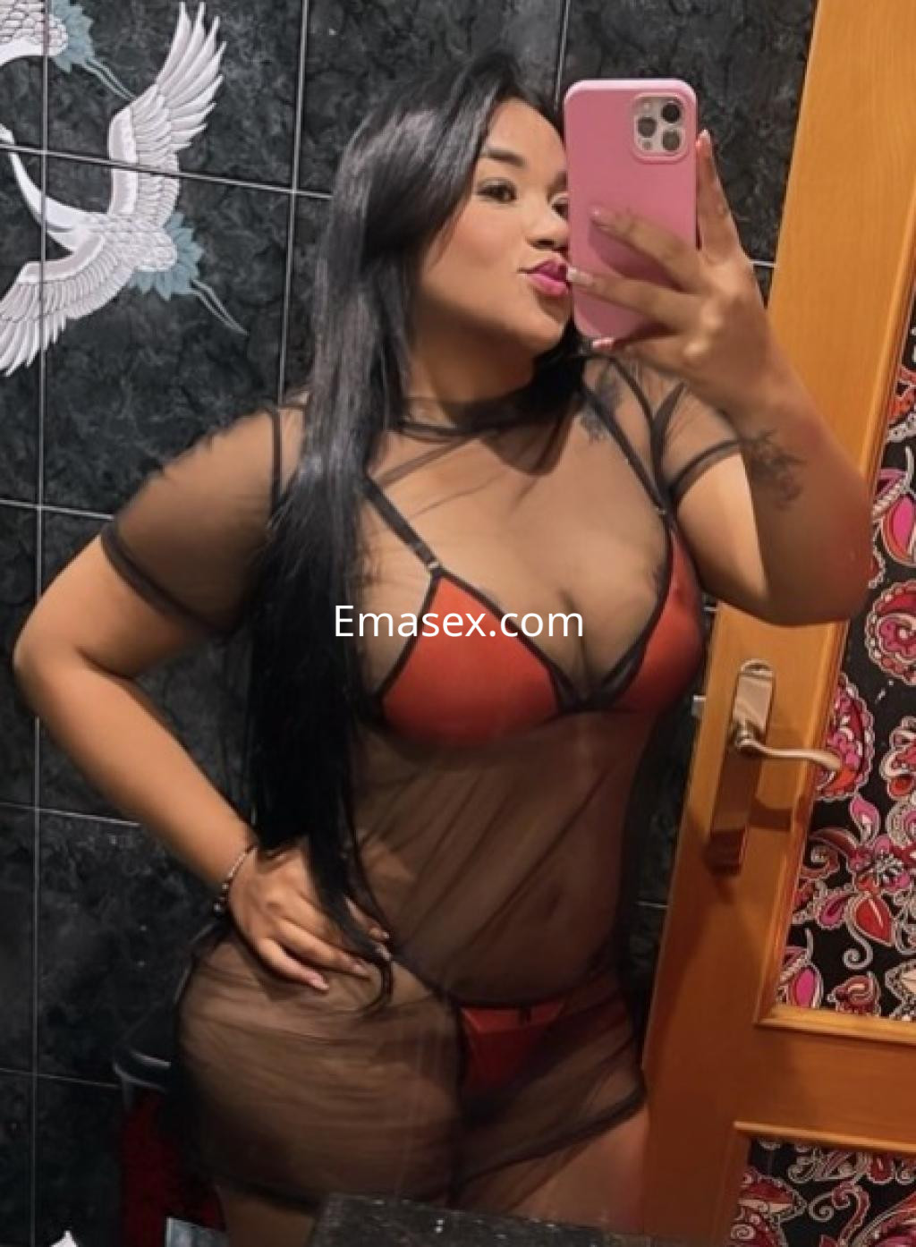 La puta en Granada posa con un conjunto de lencería roja y un vestido de malla negra, mostrando confianza.